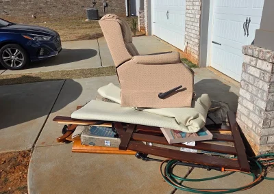 Old recliner and furniture piled in a driveway for pickup - Huntsville area junk removal