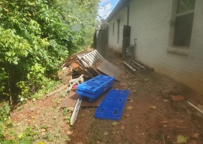 Debris along the side of a house before removal - Huntsville area junk removal